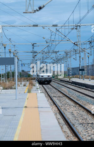 Un train arrivant en gare sur une journée ensoleillée sous de nombreux câbles et structures métalliques. Vertical image Banque D'Images