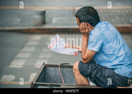 Xian, Chine - Juillet 2019 : Chinese man reading informations dépliant publicitaire tout en restant assis à l'intérieur d'un chariot à roues Banque D'Images