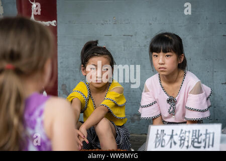 Xian, Chine - Juillet 2019 : Deux petites filles en regardant un Caucasian girl debout devant un stand de souvenirs sur la rue dans les quar Banque D'Images