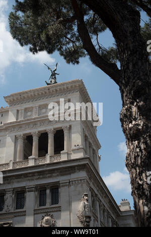 Rome, Italie - 5 juillet 2018 : un arbre frames un bâtiment très ornementé surmonté d'une statue à ailes un jour d'été à Rome. Banque D'Images