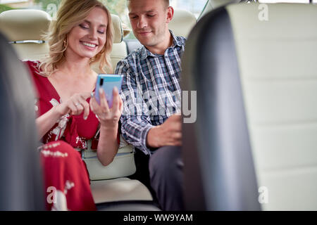 Image les femmes et les hommes avec le téléphone en mains assis sur siège arrière de voiture pendant la journée. Banque D'Images