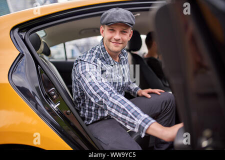 Image de l'homme heureux dans le chapeau et chemise à carreaux à la recherche de camera sitting in back seat en taxi jaune en après-midi Banque D'Images