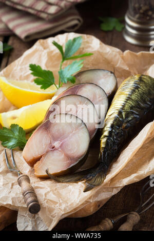 Maquereau fumé à froid de poisson coupé en tranches et servi sur un papier parchemin avec feuilles de persil frais et des quartiers de citron Banque D'Images