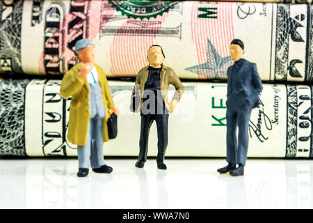 Miniatures de businessmen standing in front of american dollar billets et prendre des décisions économiques sur fond blanc Banque D'Images