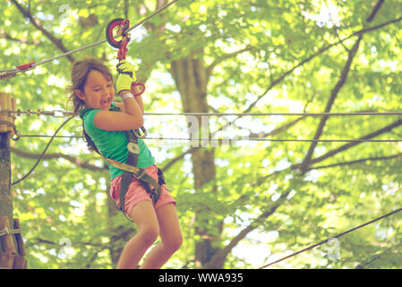 Happy little girl sur la tyrolienne entre les arbres Banque D'Images