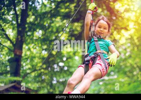 Happy little girl sur la tyrolienne entre les arbres Banque D'Images