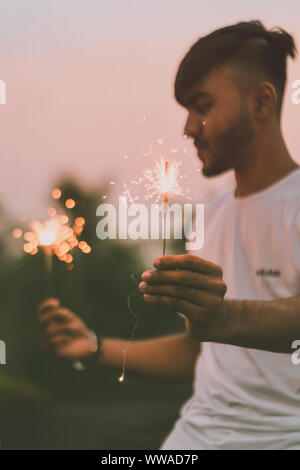 Homme hand holding burning sparkler dans les deux part célébrant Diwali ou Nouvel An avec floue fond vert. Film cinématographique avec ton aspect décoloré. Banque D'Images