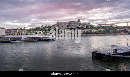 Vue du coucher de soleil du château de Buda au-dessus du Danube à Budapest en Hongrie avec une rivière passant par des navires de croisière Banque D'Images