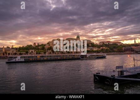 Vue du coucher de soleil du château de Buda au-dessus du Danube à Budapest en Hongrie avec une rivière passant par des navires de croisière Banque D'Images