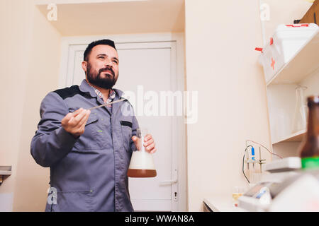 Spécialiste de la tenue de protection blanc en résille avec masque et travaillant dans l'usine d'aliments et de boissons. Spécialiste de l'homme contrôle de bouteilles pour boissons Banque D'Images