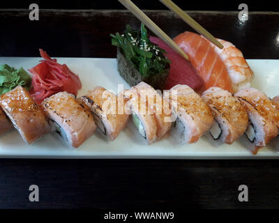 Rouleaux de Philadelphie, sushi, wasabi et gingembre carré blanc sur plaque et sur la surface de la table en bois sombre. Les baguettes sont prêts à prendre un morceau. F sélective Banque D'Images