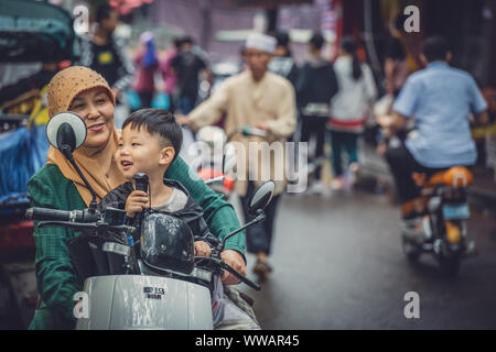 Xian, Chine - Juillet 2019 : femme musulmane avec son fils assis sur un scooter sur la route dans le quartier musulman Banque D'Images