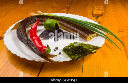 Still Life - orphie fumé avec de la chaux, le basilic, l'oignon vert, chili, nori chips, épices, huile d'olive dans un plat de céramique blanc, sur une table en bois Banque D'Images