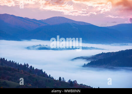 Campagne automne merveilleux dans les montagnes à l'aube. vallée pleine de froid brouillard flottant au-dessus du ciel rougeoyant. ridge lointain. champs agricoles sur rolli Banque D'Images