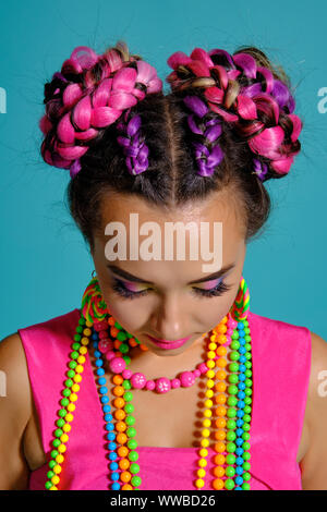 Jolie fille avec une coiffure tresses multicolores et lumineux maquillage, posant en studio sur un fond bleu. Banque D'Images