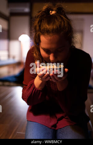 Jeune femme assise en seiza touristiques caucasienne restaurant japonais traditionnel nuit noire prix dans un ryokan, holding tasse de thé vert sencha Banque D'Images