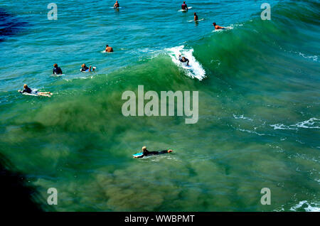 Huntington Beach, Californie / USA - 7 septembre, 2019 : Surfer rides une vague tandis que ses collègues surfeurs attendre la prochaine vague. Ombre portée par les spectateurs sur le quai. Banque D'Images