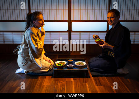 Jeune couple assis seiza sur marbre coussins avec ryokan japonais plats kaiseki, manger nouilles soba, natto, edamame et sauce de soja sur la table par slidin Banque D'Images