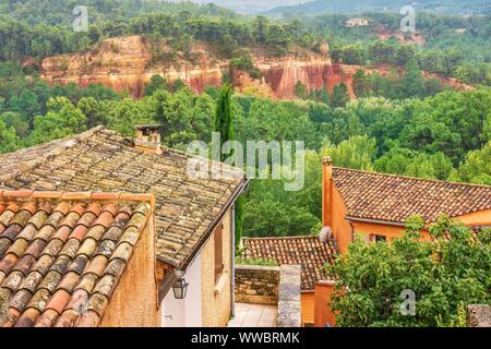 En Roussillon, France, maisons faites de la région, de couleur ocre, avec l'ancienne carrière dans l'arrière-plan, comme forêt retourne à la mine fermée. Banque D'Images