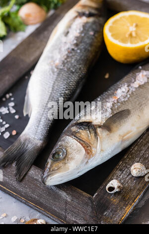 Loup de mer frais prêts à cuire. Le poisson avec le persil, le citron et rose sel de l'Himalaya. Le concept de la saine et une bonne nutrition. Banque D'Images