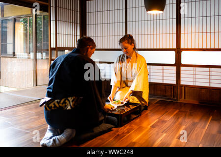 Couple homme et femme en kimono assis seiza manger des aliments à la maison traditionnelle japonaise ou ryokan prix par table avec plaques de légumes sautés par shoji Banque D'Images