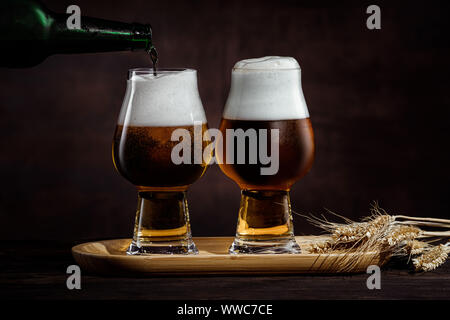 Deux verres de bière noire froide et épillets de blé sur fond sombre. Banque D'Images