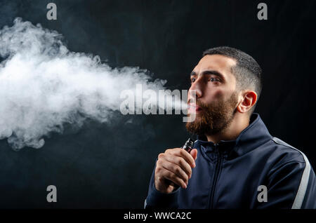 homme tenant la cigarette électronique ou la cigarette électronique de forme vaque avec de la fumée blanche sur fond noir. Banque D'Images