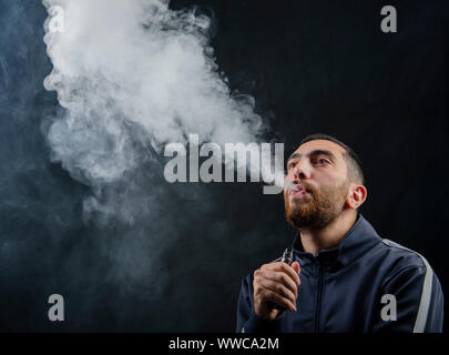 homme tenant la cigarette électronique ou la cigarette électronique de forme vaque avec de la fumée blanche sur fond noir. Banque D'Images