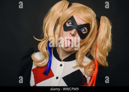 Une jeune fille dans un costume et une perruque sur un fond noir est souriant et montrant la langue. Cosplay Girl caractère Harley Quinn et s'amuser dans la salle de studio Banque D'Images