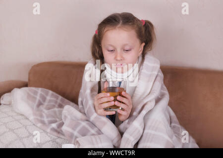 Enfant prenant la médecine. Sick girl avec écharpe lying on bed Banque D'Images