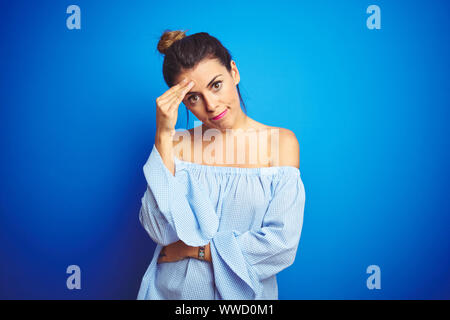 Belle Jeune femme portant bun hairstyle sur fond isolé bleu inquiet et a souligné à propos d'un problème avec la main sur le front, nerveux et anxi Banque D'Images