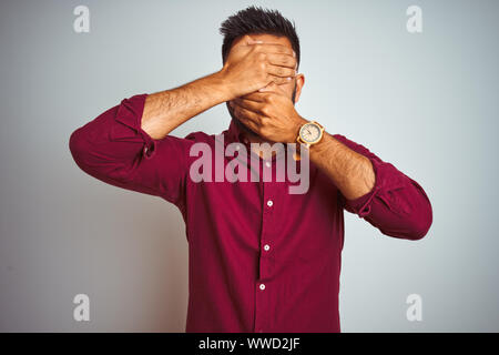 Jeune Indien man wearing red shirt debout sur fond gris isolées couvrant les yeux et la bouche avec les mains, surpris et choqué. La clandestinité em Banque D'Images