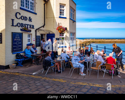 Une foule de personnes de manger à l'extérieur de la cod et pub de homard sur le port à Staithes Yorkshire du Nord à l'automne Banque D'Images