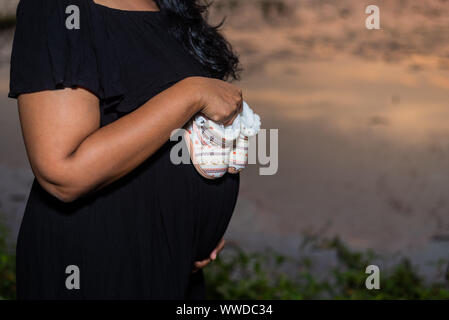 Pregnant woman in black gown holding baby boots et affiche son bébé au tournage d' Banque D'Images