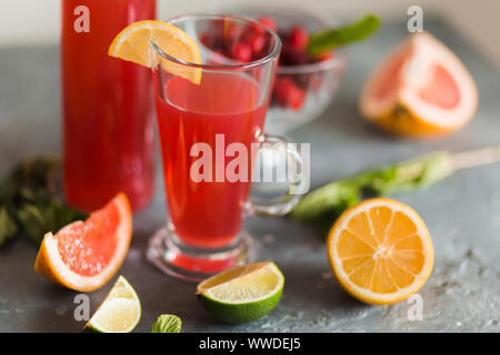Libre de limonade rose rouge dans un verre transparent et une bouteille d'agrumes, de menthe et de cranberry sur la table de la cuisine. Citron, pamplemousse, citron vert à côté d