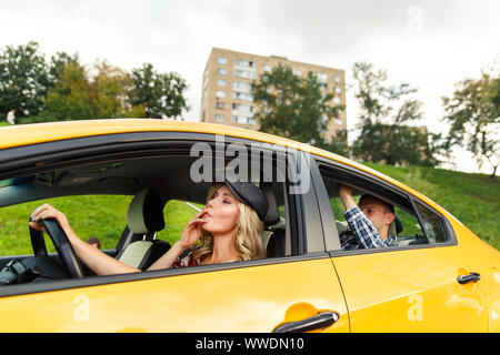 Photo de femme pilote avec cigarette et passager en taxi jaune en après-midi Banque D'Images