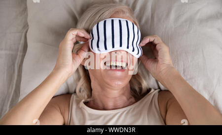 Happy smiling mature woman sleeping mask Lying in Bed Banque D'Images