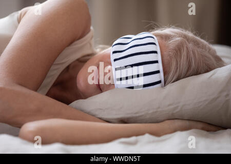 La maturité calme femme portant un masque de sommeil relaxing in bed Banque D'Images