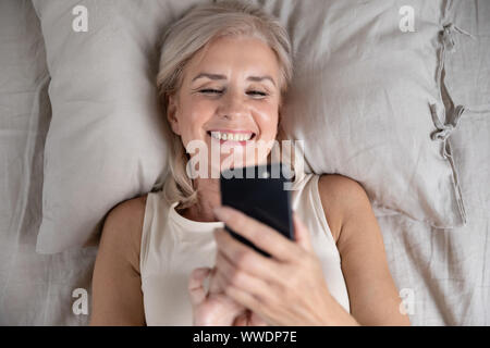 Happy smiling mature woman having fun with cellphone vue supérieure