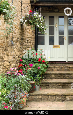 Joli escalier en pierre menant à la porte de la chambre avec des jardinières, corbeilles suspendues et les plantes à fleurs, Easton sur la Colline,Northamptonshire, Angleterre, Royaume-Uni Banque D'Images