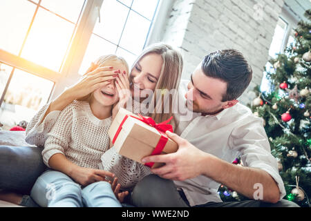 Portrait de jeune famille heureuse. mère couvre ses yeux de fille en tant que père va faire surprise pour Fille donne à présent, près de l'arbre de Noël. Ha Banque D'Images