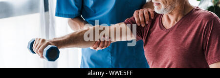 Vue panoramique tourné de médecin, debout près de man exercising with dumbbell in clinic Banque D'Images
