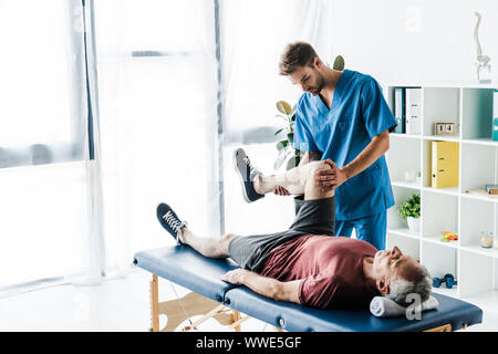 Beau médecin touchant de jambe mature patient couché sur la table de massage Banque D'Images