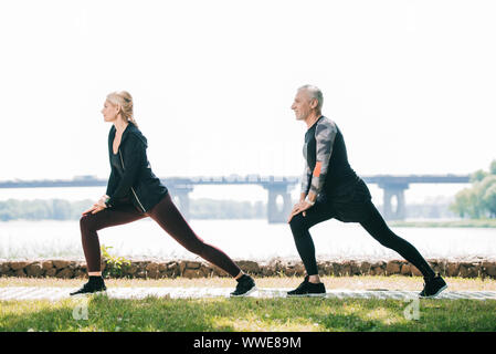 Vue latérale du sportif et de la sportive mature faisant se jette exercices sur riverside en park Banque D'Images