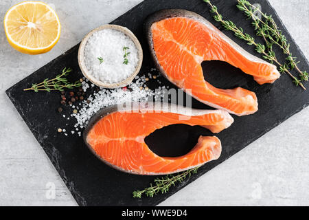 Deux steaks de saumon cru, sel de mer, thym et citron pour la cuisson du poisson grillé sur fond d'ardoise noire. Vue d'en haut Banque D'Images