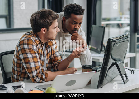 Programmeur sérieux gesturing while looking at computer monitor avec african american collègue Banque D'Images