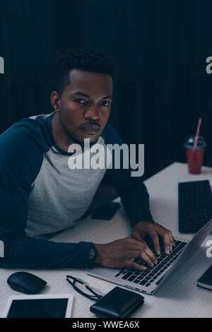 African American programmer looking at camera tout en travaillant de nuit in office Banque D'Images