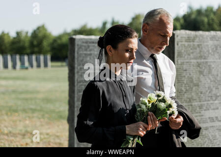 Senior homme barbu près de femme avec des fleurs sur funeral Banque D'Images