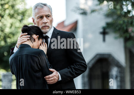 Sad man hugging contrarié femme près de l'église Banque D'Images