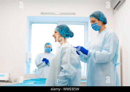 L'infirmière met le patient dans une blouse stérile pour l'opération. L'élimination des taupes dans une clinique privée. Banque D'Images